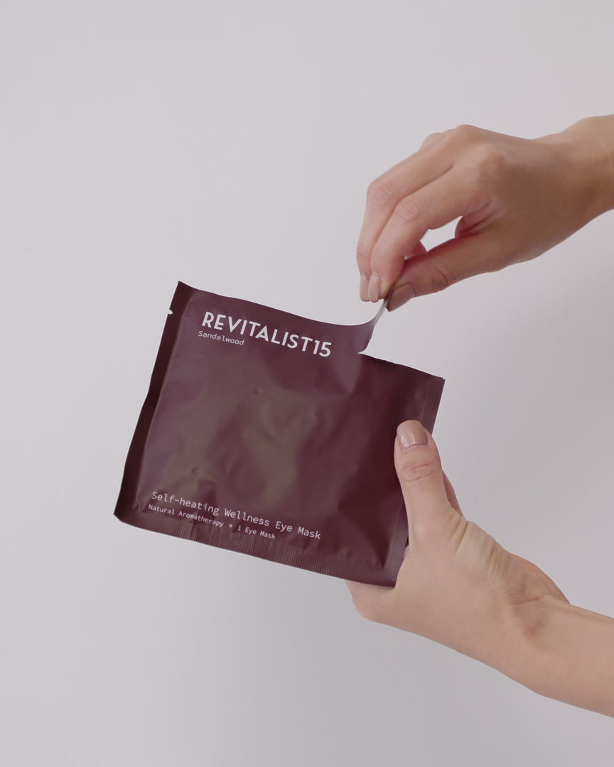 Hands opening a Revitalist15 self-heating eye mask pouch, showing how to open and the pouch and remove the mask before use.