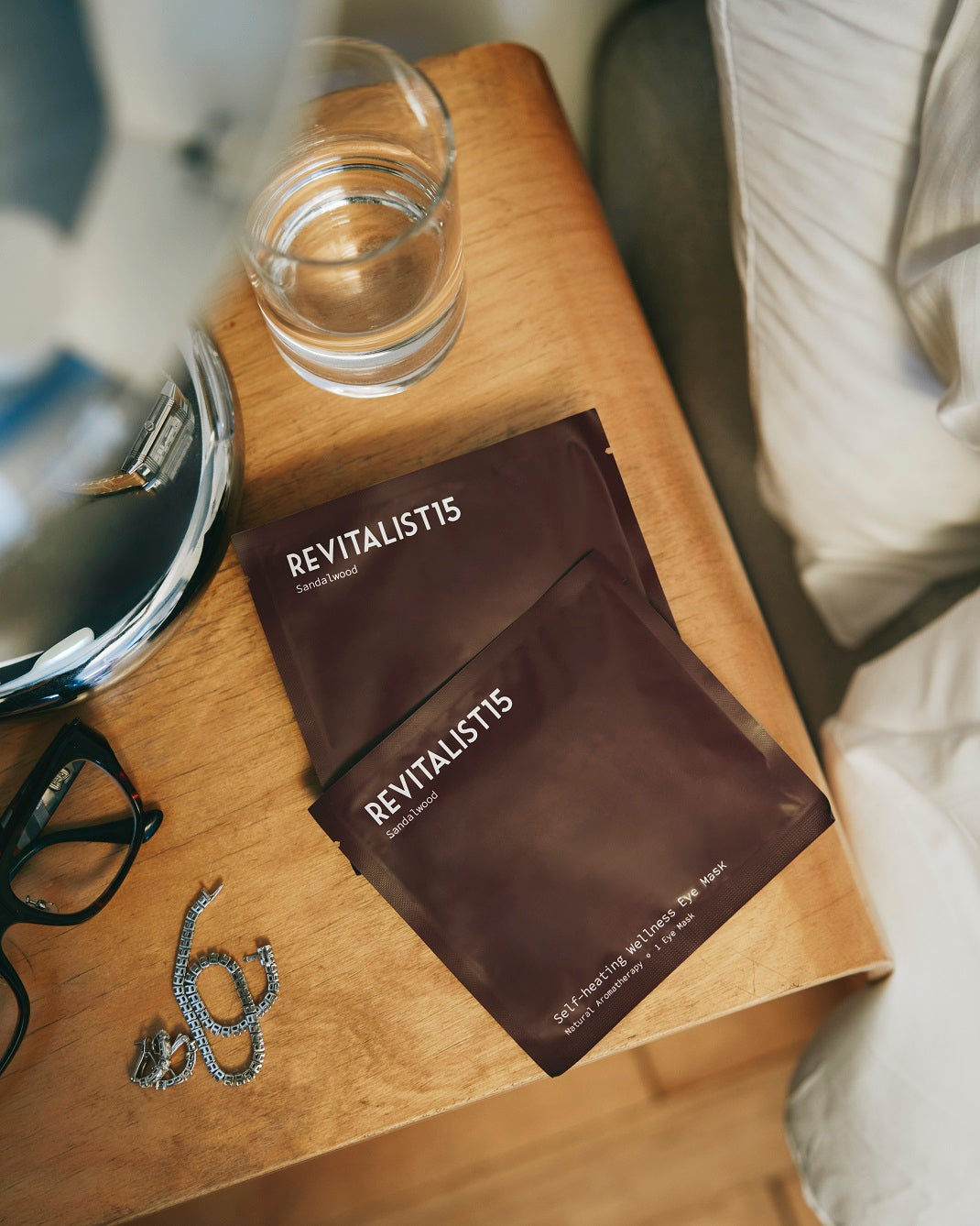 Revitalist15 self-heating sandalwood eye mask and packaging displayed on a nightstand, evoking calm and nightly ritual.
